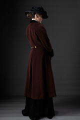 A Victorian or Edwardian woman wearing a winter coat and hat against a studio backdrop