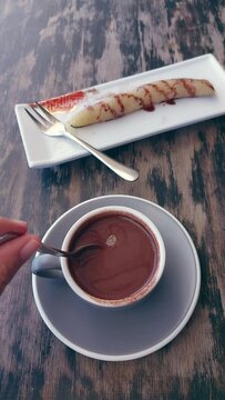 Vertical POV handheld view of hand leisurely stirring a cup of sikwate or tsokolate that is a Filipino chocolate drink to be paired with suman for an authentic traditional merienda in the Philippines