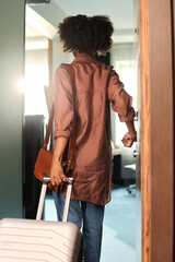 Vertical back view of young African American woman opening door to hotel room and holding suitcase