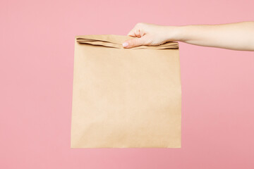 Close up cropped delivery girl female hold in hand brown clear blank craft paper bag isolated on...