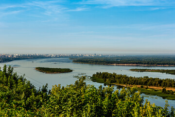 Obraz premium Samara city (Russia) on the banks of the Volga River. High buildings, blue water, forest, tree, bush. Quiet summer morning with light sky.