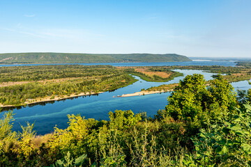 Zhiguli Mountains, Volga River and quiet backwater near the city of Samara, Russia. Blue water, sandy shore, tree, bush, ship. Quiet summer morning with light sky.