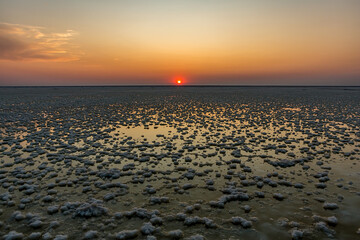 Sunset or sunrise on salt lake Elton (Russia) with mirror or reflection of low Cumulostratus or Stratocumulus clouds in the brine at golden hour with the sun in the background. Evening or morning.