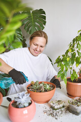 In a cozy room, a smiling woman tends to her beloved plants with care, creating a green oasis in...