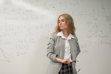 A Caucasian woman stands at a blackboard with written formulas.