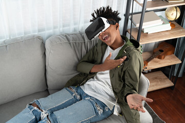 Surprised African American looking VR enjoy watching leaning back sofa by touching air in fantastic...
