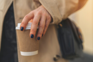 hand of femail holding paper cup of take away coffee outside toned image