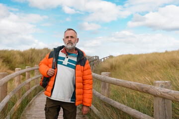 happy bearded man with backpack reaching destination on seaside in Wales on warm Autumn day 
