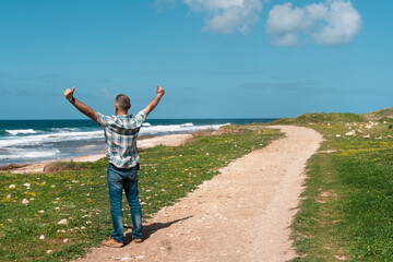 happy man reaching destination, rising hands  on seaside on warm sunny day