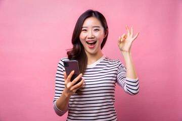 Woman excited holding mobile phone and gesturing ok sign, studio shot isolated on pink background