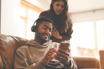 woman  beside herself peeking into phone of man sitting on couch at home