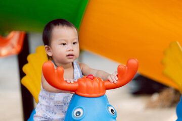 Portrait of little boy playing with colorful spring rocking horse in the playground. In a moment of...