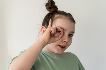 A little girl holds a lollipop pill near her eye. Happy girl in green t-shirt on white background.
