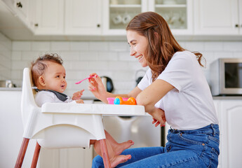 Happy mother, kitchen and feeding baby with spoon on high chair for meal, snack time or breakfast at home. Mom with infant, newborn or child for food, nutrition or care with love or support at house