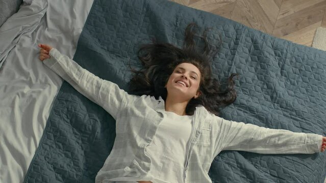 Top view Caucasian Young woman brunette fall on bed rest pleasure happiness smile laughter fun girl bedroom domestic lifestyle carefree lady enjoy positive relaxed lying soft mattress cozy comfortable