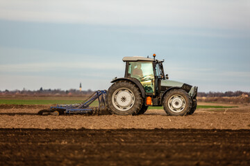 Tractor with a plow attachment tilling the soil in a vast farmland setting