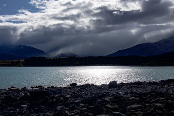 The setting sun over Lake Tekapo in New Zealand with ominous clouds coming over the mountains
