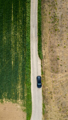 Obraz premium Aerial shot of a car on a narrow road splitting two contrasting fields, vibrant green and dry yellow.
