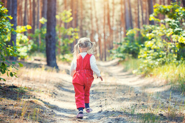 Portrait of smiling three years old caucasian child girl runs on the trail in the pine forest....