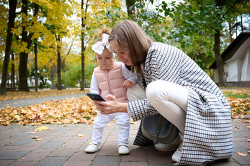 Mother and cute baby girl walking in autumn park with leaves on the ground. Mom spending time with...