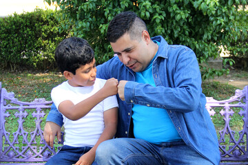 Divorced single dad on a park bench with his 10-year-old dark-skinned Latino son spending quality time and celebrating Father's Day