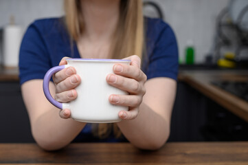 Kobieta siedzi przy stole i trzyma duży kubek z mlekiem