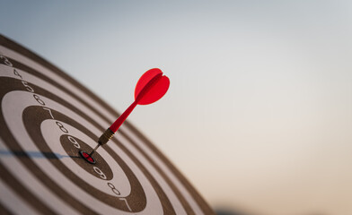 Close up shot red darts arrows in the target center on dark blue sky background. Business target or...