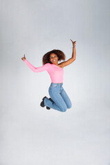 Obraz premium Chica negra feliz. Mujer negra saltando. Mujer saltando sonriendo con los brazos abiertos. Publicidad. Cartelería. Rosa y vaquero