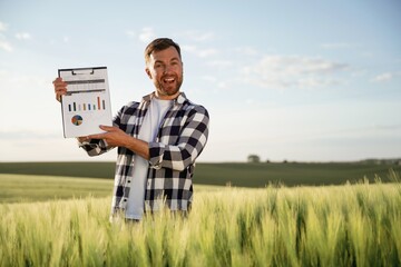 Successful businessman with graphs on notepad is standing on the agricultural field at daytime