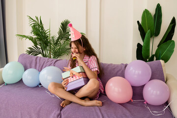 Girl laughing with party hat and holding birthday gifts.