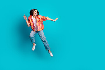 Full size photo of nice young girl jump fight empty space wear plaid shirt isolated on teal color...