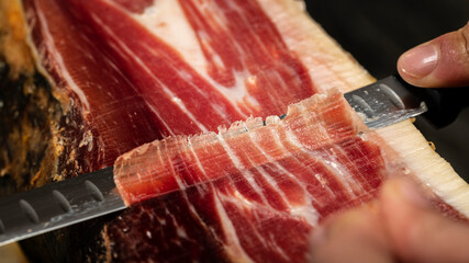 Iberian acorn fed ham. Close-up of ham knife cutting a thin slice of Iberian ham of Spanish origin....