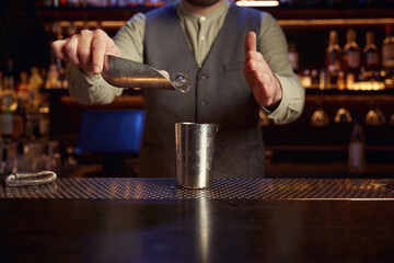 Bartender pouring ice cubes into steel shaker standing at bar counter