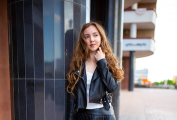 Fototapeta premium A young smiling girl in a good mood walks around the city. Teenage girl, portrait against the background of houses and roads. Fashionable youth style trend.
