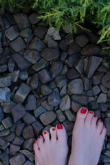 bare female feet with red nail polish stand on pebbles in the park