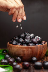 A wooden bowl filled with 'Indian blackberry' or Jamun (Syzygium cumini) fresh fruits, sprinkled...