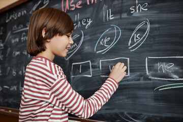 Medium shot of Caucasian schoolboy wearing casual clothes writing on blackboard in English class, copy space