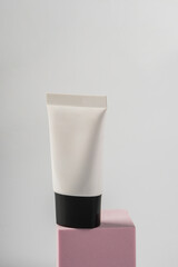 Plastic white tube for cream or lotion. Skin care or sunscreen cosmetic with stylish props on white background.