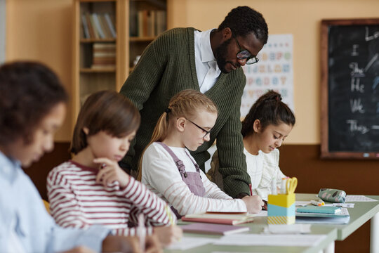 African American male teacher of English working in class watching kids doing writing exercise