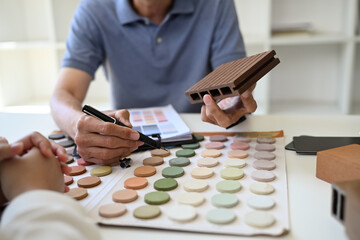 Closeup professional interior designer helping client choosing colors in swatches palette for...