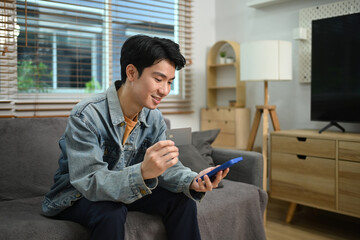 Handsome young man holding credit card using internet banking application on his smartphone
