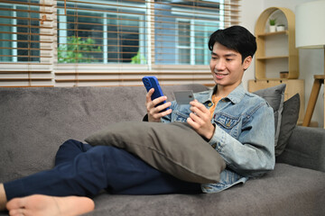 Happy young Asian man holding credit card making payment on mobile phone. Internet banking and...