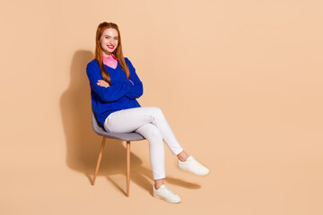 Full length portrait of pretty young lady crossed arms sit chair wear sweater isolated on beige...