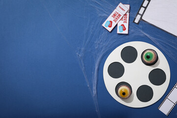 Reel, paper films, tickets and jelly eyes on blue background, space for text