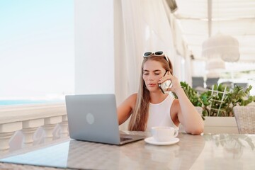 Woman coffee cafe laptop. Coffee break in cafe with sea view. Tranquil long haired woman drinking coffee in plant filled place. Woman sitting at a coffee shop with mobile phone drinking coffee.