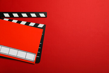 Clapperboard and red paper with film on red background, space for text