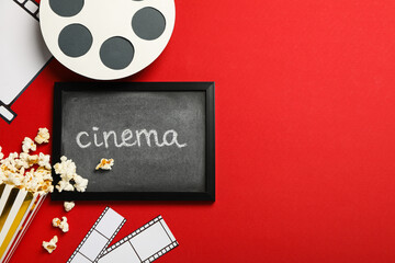 Blackboard with text, paper cup with popcorn, film and reel on red background, space for text