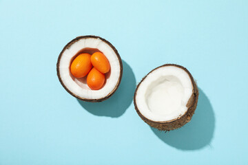 Two half of coconut and whole kumquat on blue background, top view
