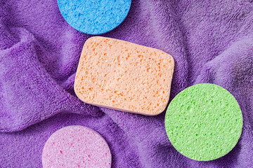 Top view of purple towel and different kinds of sponges for daily  and gentle exfoliating