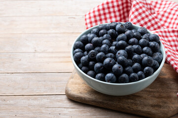 Blueberries in green bowl on wooden table. Copy space